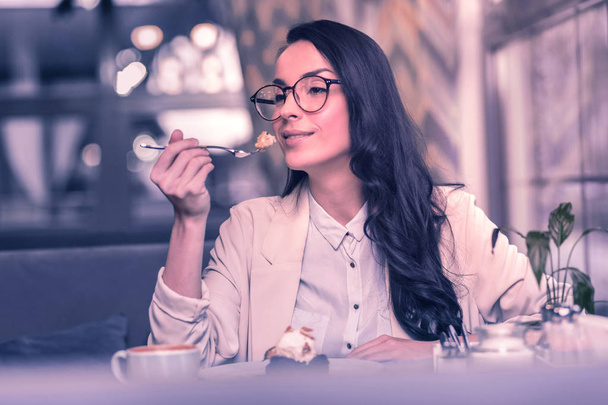 Delicious dessert. Beautiful nice woman taking a piece of cake while sitting in the cafeteria - Фото, изображение