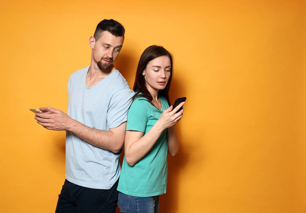 Νεαρό ζευγάρι με τα κινητά τηλέφωνα σε χρώμα φόντου - Φωτογραφία, εικόνα