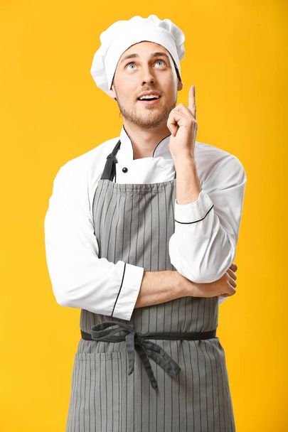 Handsome male chef pointing upwards on color background - Photo, Image