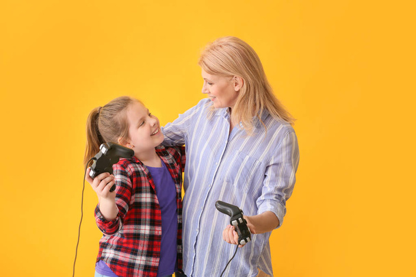 Kypsä nainen ja hänen söpö tyttärentytär pelaa videopeli värillinen tausta
 - Valokuva, kuva