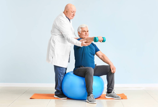 Senior fysiotherapeut werken met volwassen man in kliniek - Foto, afbeelding