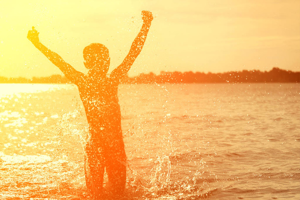 Sziluettje a gyermek fröccsenő a vízben. Fiú játszik a tengerben. Gyerek szórakozik a szabadban. Nyári vakáció és egészséges életmód koncepció. - Fotó, kép