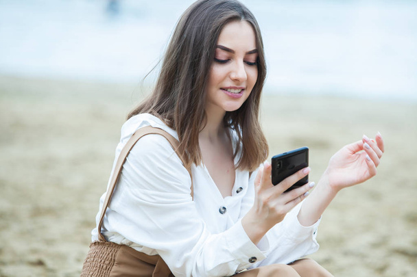 Meisje buiten texting op haar mobiele telefoon. Meisje met telefoon. Portret van een gelukkige vrouw tekst SMS-bericht op haar telefoon. - Foto, afbeelding