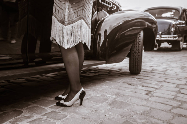 古いオートの近くに女性の足。ハイヒールの靴を履いた若い女性. - 写真・画像