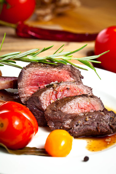 gourmet grilled venison fillet with tomatoes and rosemary on wooden table - Photo, Image