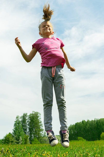 Holčička skáče a hraje na zelené louce v parku. Letní koncept, dětské hry v čerstvém vzduchu. - Fotografie, Obrázek
