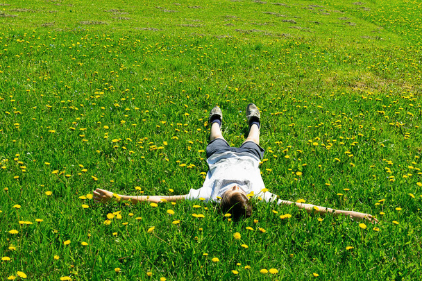 Dospívající chlapec leží na zelené louce v čerstvé trávě parku. Letní koncept, dětské hry v čerstvém vzduchu. - Fotografie, Obrázek