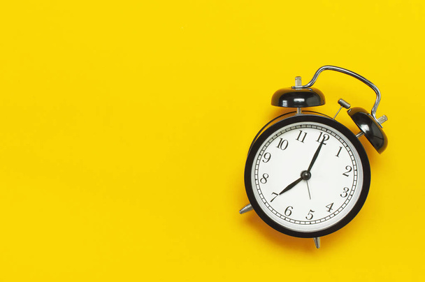 Reloj despertador retro negro con vista superior de fondo amarillo Espacio plano para copias. Antecedentes minimalistas, concepto de tiempo, plazo, tiempo para trabajar, mañana
 - Foto, imagen