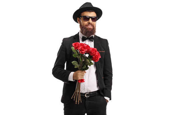 Bearded man in a suit holding a bouquet of red roses isolated on white background - Foto, immagini