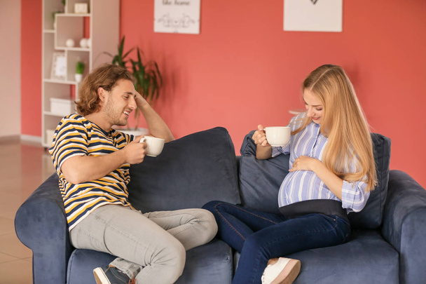 Feliz joven embarazada pareja bebiendo té en casa
 - Foto, imagen