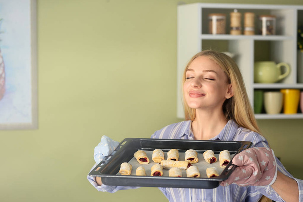 Woman holding baking tray with homemade pastry in kitchen - Photo, Image