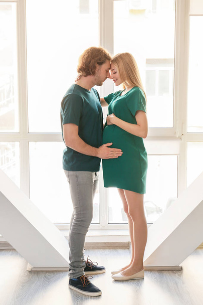 Happy young pregnant couple near window - Valokuva, kuva