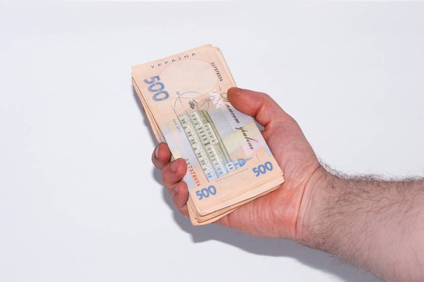 Geld in mannelijke hand op een witte achtergrond, Oekraïense Hryvnia een grote bundel van rekeningen, close-up, kopieerruimte - Foto, afbeelding