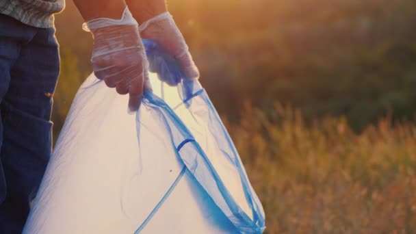 Gloved mensen opruimen in de natuur, zet flessen in een zak - Video