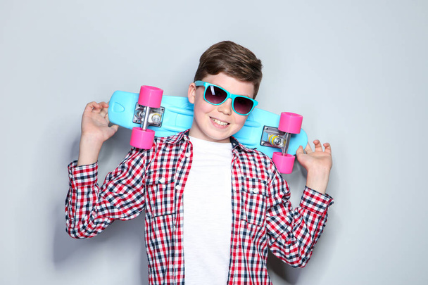 Young boy in sunglasses holding skateboard on grey background - Foto, Imagem