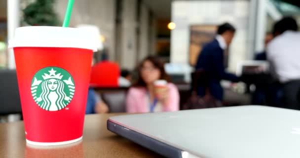 disposable red cup of starbucks coffee with laptop on table and people on background - Video, Çekim