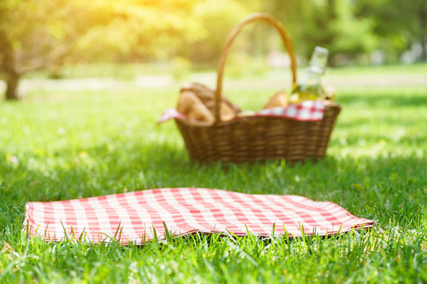 Wicker picnic basket with food and red tablecloth on the grass. - 写真・画像