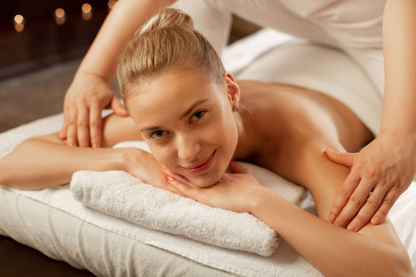 Sorrindo menina nua de boa aparência deitada em toalhas brancas enquanto mestre de massagem
 - Foto, Imagem