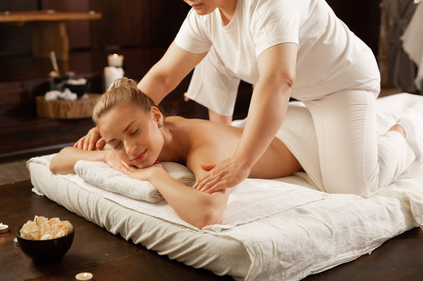 Masseuse in white uniform sitting on the back of her client - Photo, Image