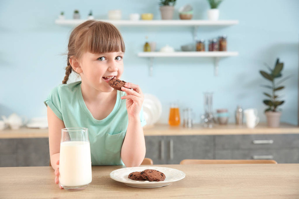 Schattig klein meisje met glas melk en koekjes aan tafel - Foto, afbeelding