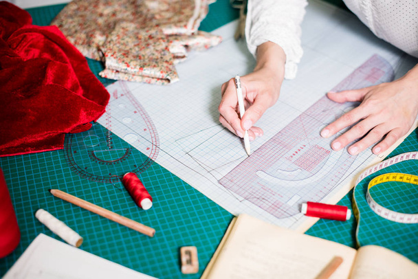 Handen van Lady Tailor werken in haar atelier, gereedschap en stof stalen op de naai tafel - Foto, afbeelding