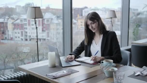 pretty woman making notes in a notebook. Young businesswoman Sitting in coffee shop at wooden table. On table is gray aluminum laptop. Schedules and makes important notes - Footage, Video