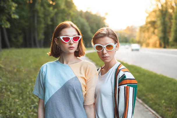 Дві модні молоді жінки, що йдуть по вулиці на заході сонця
 - Фото, зображення