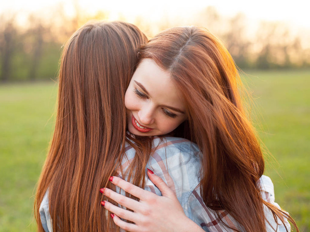 Dwie młode kobiety przytulają się na zielonym polu - Zdjęcie, obraz