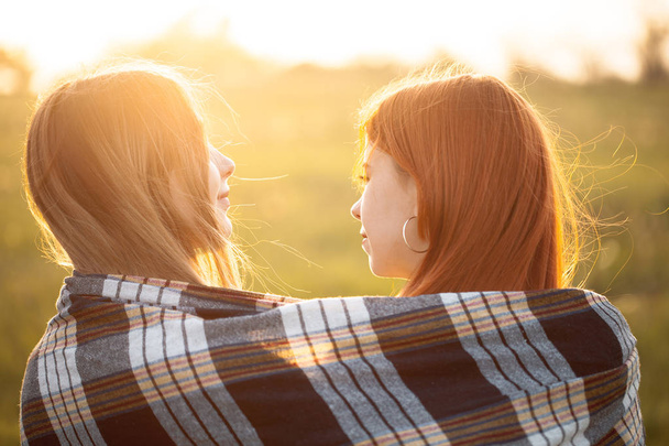 Δύο κορίτσια καλυμμένα με κουβέρτα που στέκονται μαζί κάτω από το ηλιοβασίλεμα. Καλύτεροι φίλοι. - Φωτογραφία, εικόνα