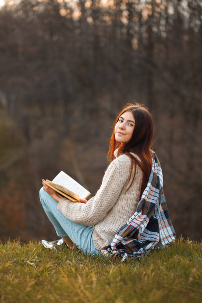Una giovane donna si siede all'aperto e legge un libro la sera. Girati.
. - Foto, immagini