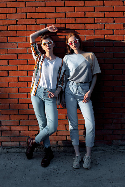 Two young women standing near the brick wall - 写真・画像