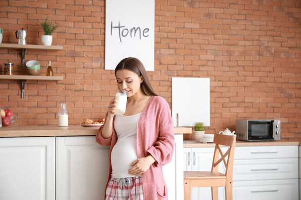 Piękna kobieta w ciąży picie smaczne mleko w kuchni w domu - Zdjęcie, obraz