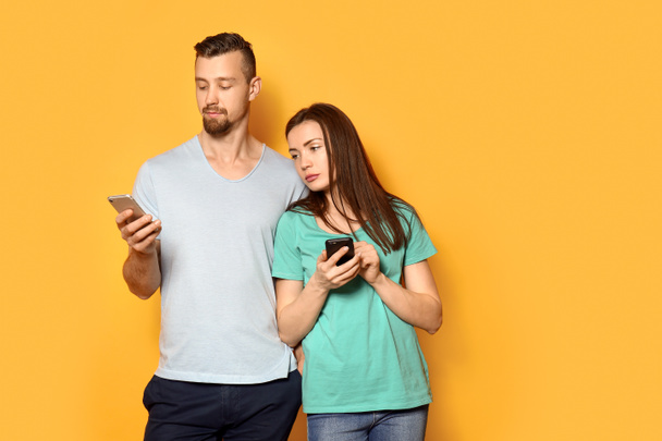 Νεαρό ζευγάρι με τα κινητά τηλέφωνα σε χρώμα φόντου - Φωτογραφία, εικόνα
