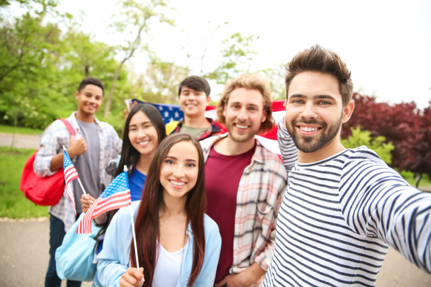 Grupo de estudiantes con bandera de EE.UU. tomando selfie al aire libre
 - Foto, Imagen