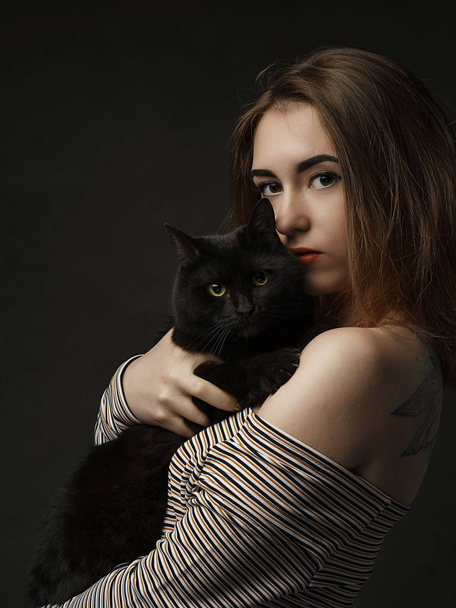 Beautiful sexy woman in black holding black cat. Beautiful young and stylish woman holding a gray cat. Studio photo. art - Foto, Imagen