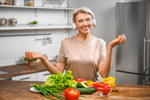 Зрелая женщина слушает музыку во время приготовления пищи на кухне
 - Фото, изображение