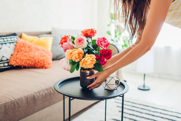Frau stellt Vase mit Blumenrosen auf den Tisch. Hausfrau kümmert sich um Gemütlichkeit in der Wohnung. Interieur und Dekoration - Foto, Bild