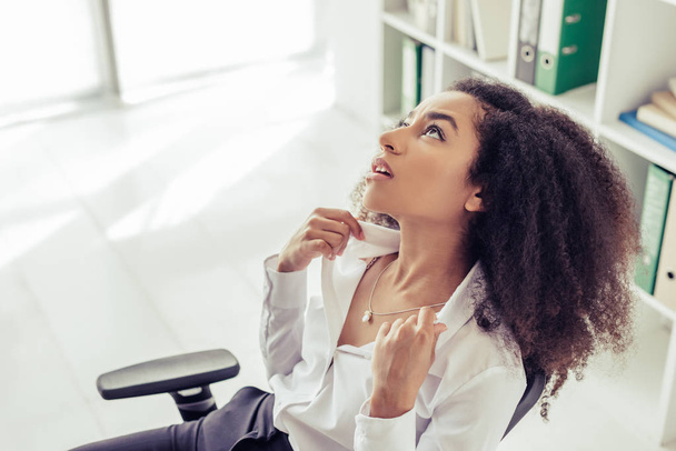exhausted african american businesswoman looking up while suffering from summer heat in office - 写真・画像