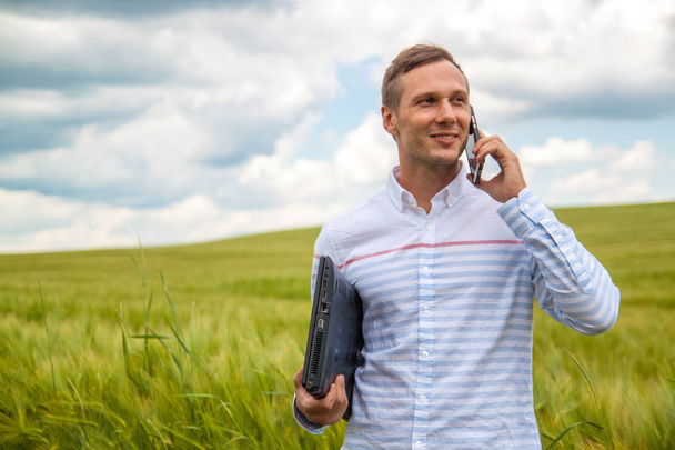 homme d'affaires avec ordinateur portable et smartphone travaillant dans le champ de blé en fond bleu ciel
. - Photo, image