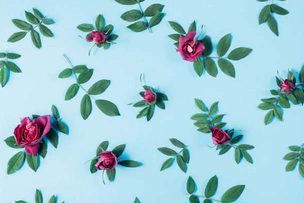 Summer minimal concept. Pattern made of red rose flowers and green little leaves on blue background. Many little leaves for decorating any post card or celebration card. Flat lay, top view - Fotó, kép
