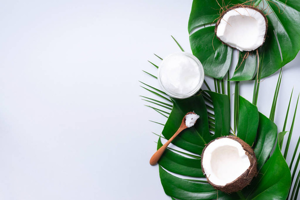 Green tropical monstera leaves, ripe coconuts, coconut oil on grey background with copy space. Top view. Summer creative layout. Skin care cosmetics. Hair, body treatment - Foto, imagen