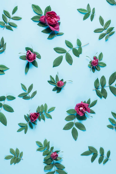 Floral pattern made of red roses, green leaves, branches on pastel blue background. Flat lay, top view. Nature background. Pattern of flowers. Flowers pattern texture - Fotó, kép