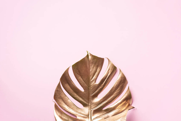 Exotic summer trend in minimal style. Golden tropical palm monstera leaf on pastel pink color background. Shiny and sparkle design, fashion concept. - Fotó, kép