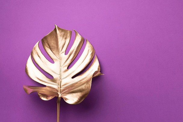 Exotic summer trend in minimal style. Golden tropical palm monstera leaf on violet color background. Shiny and sparkle design, fashion concept. - Zdjęcie, obraz