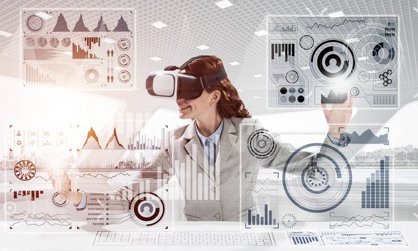 Beautiful and young business woman in suit using virtual reality headset with digital media structure while standing inside bright office. Up to date technologies - Foto, immagini