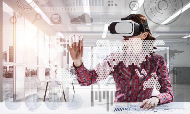 Modern technologies for education by means of young female student in checkered shirt using virtual reality goggles and interracting with digital media interface. - Foto, Bild