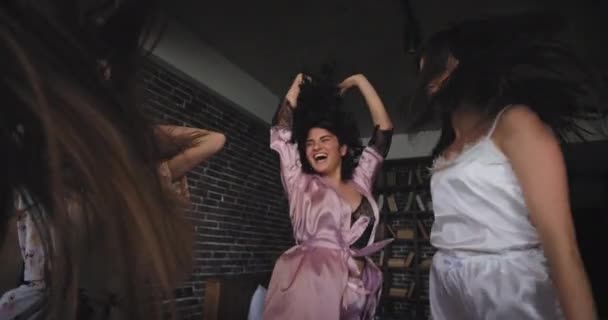 Grupo de mejores amigas damas muy atractivas en pijamas bailando y sintiéndose felices celebrando despedida de soltera en casa en un moderno estudio de diseño
 - Metraje, vídeo