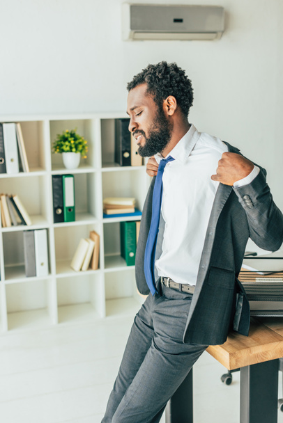 exhausted african american businessman undressing while suffering from heat in office - Photo, Image