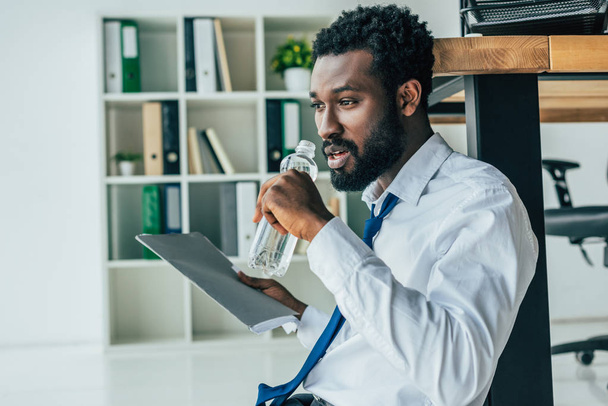 kimerült afro-amerikai üzletember iszik vizet, miközben szenved a hő - Fotó, kép