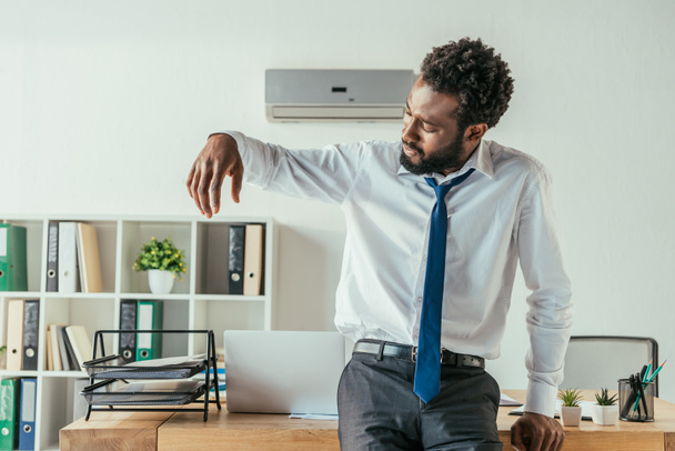 δυσαρεστημένος Αφρικανός Αμερικανός επιχειρηματίας κοιτάζοντας ιδρωμένο πουκάμισο, ενώ υποφέρει από τη θερμότητα του καλοκαιριού - Φωτογραφία, εικόνα